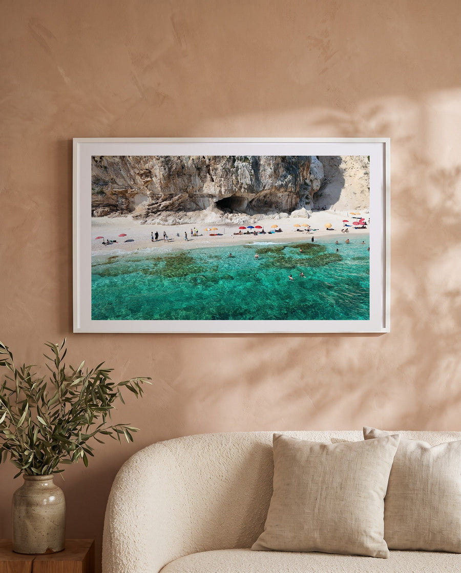 Beneath the Cliffs, Sardinia print in a white frame above a cream boucle sofa on a warm plaster wall
