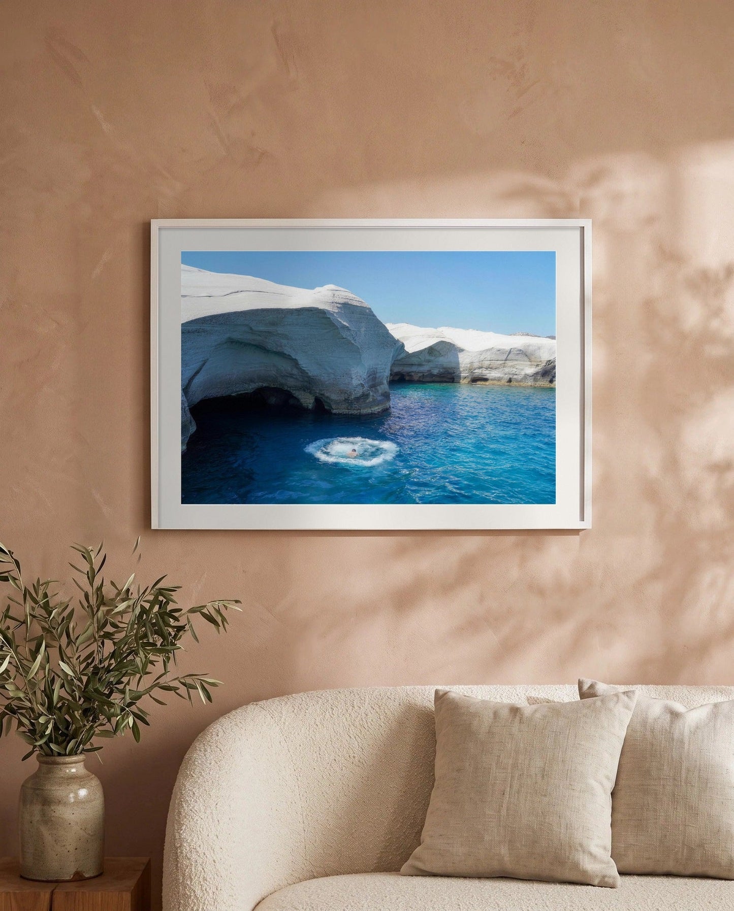 Milos Beckons framed in white above a cream boucle sofa on a warm plaster wall