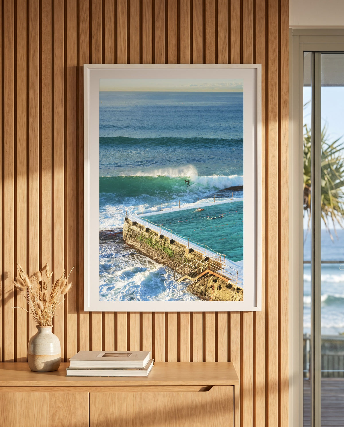Surfing at Bondi Icebergs, framed on a timber slat wall in a coastal living room (styled interior)