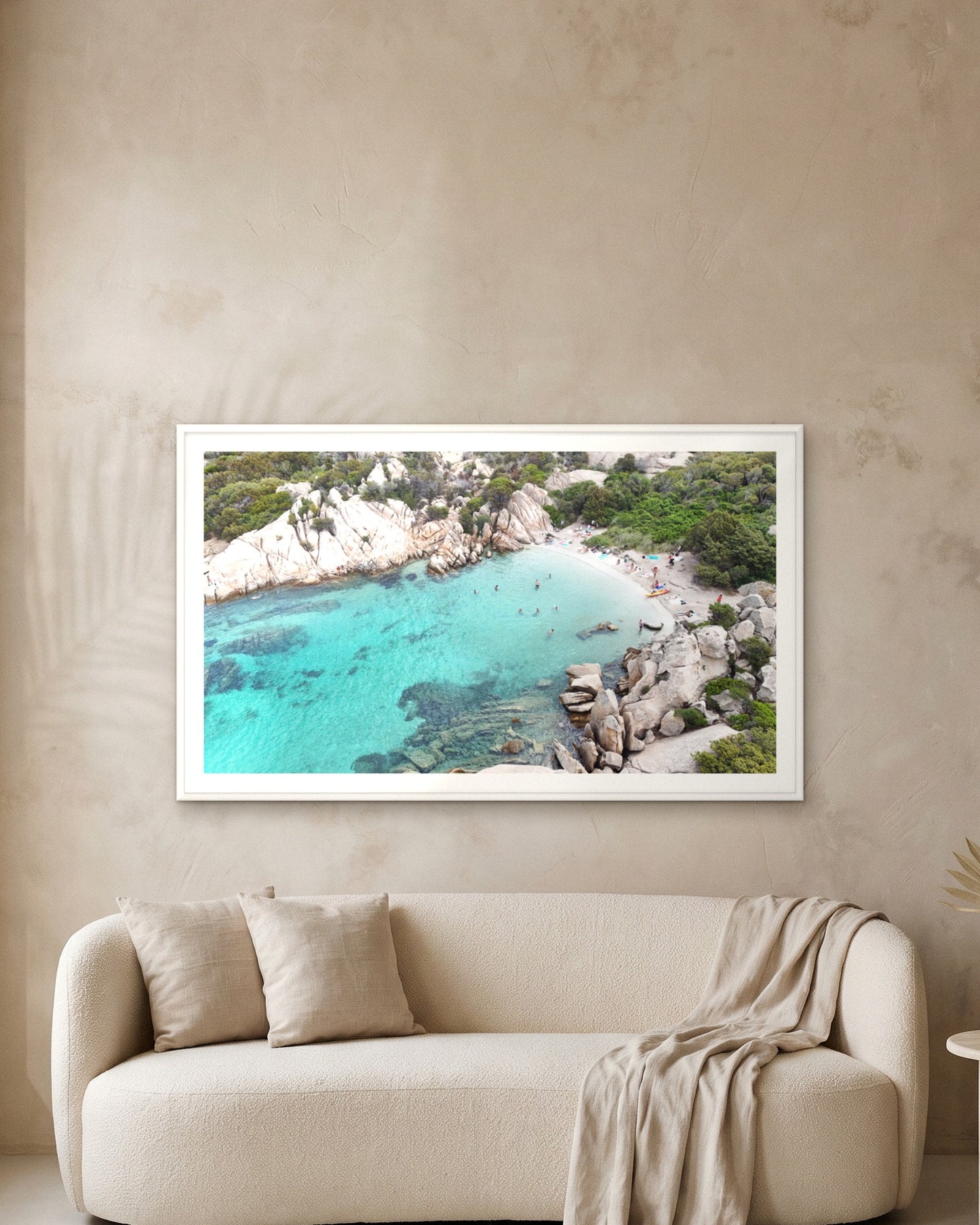 
                  
                    Hidden Beach, Sardinia, framed with a 5 cm white border above a cream boucle sofa on a textured plaster wall
                  
                