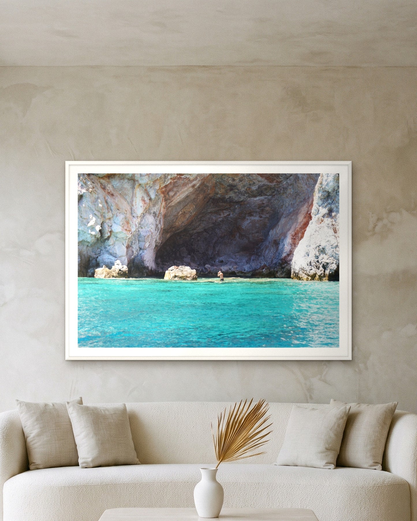 
                  
                    Kleftiko Cave, Milos, framed with a 5 cm white border above a cream boucle sofa on a textured plaster wall
                  
                