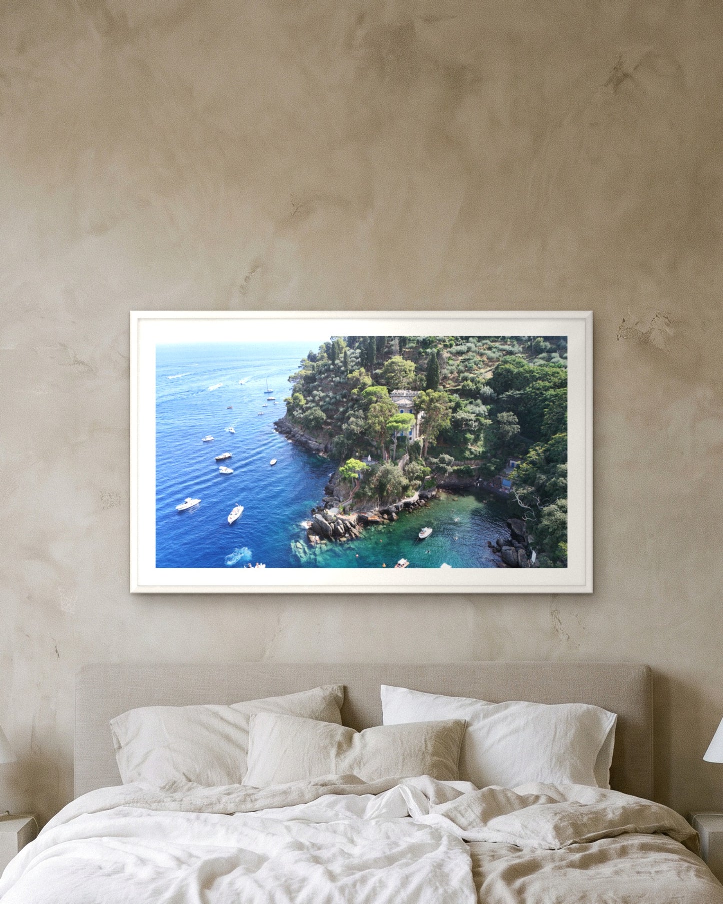 
                  
                    The Point, Portofino, framed with a 5 cm white border above a bed with linen bedding on a textured plaster wall
                  
                