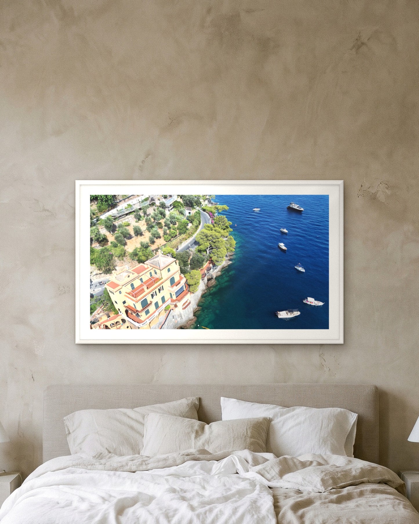 
                  
                    Villa by the Sea, Portofino, framed with a 5 cm white border above a bed with linen bedding on a textured plaster wall
                  
                
