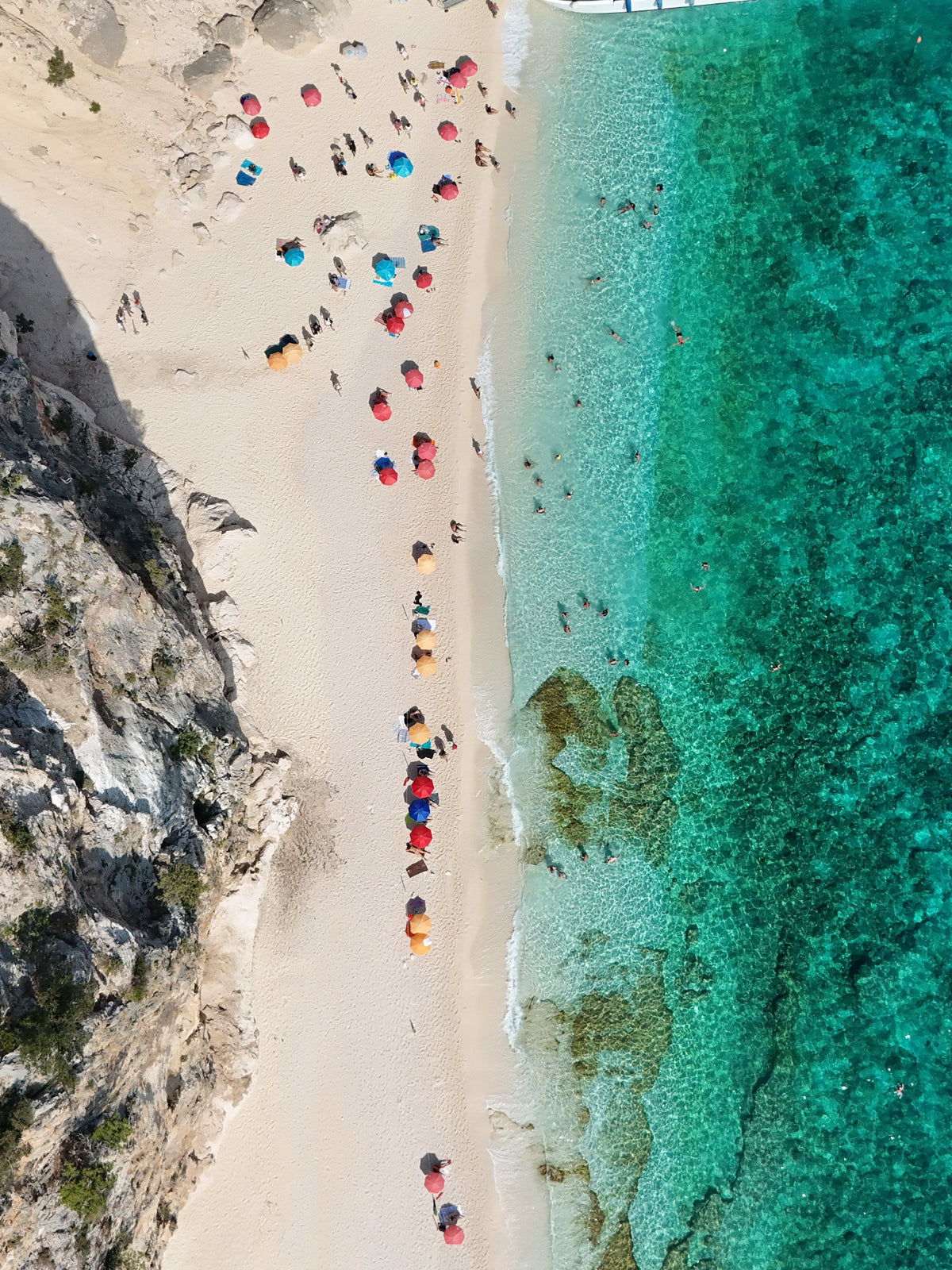 Umbrellas along a narrow Sardinian beach from above