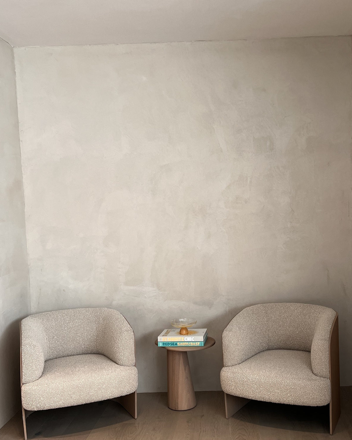 A bare plaster wall above two armchairs, before any art